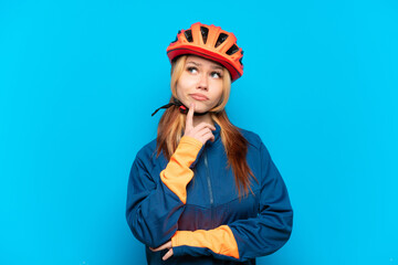 Young cyclist girl isolated on blue background having doubts while looking up
