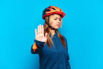 Young cyclist girl isolated on blue background making stop gesture and disappointed