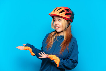 Young cyclist girl isolated on blue background with surprise expression while looking side