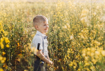 Little boy having fun and waves his hands to the camera in nature in the summer. Cute adorable child in an oilseed rape field, close portrait