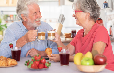 Caucasian couple having breakfast at home. Senior people relaxed and happy, holding a coffee and milk cup