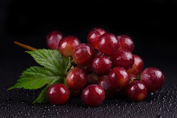 Juicy red grapes on a black background in drops of water.