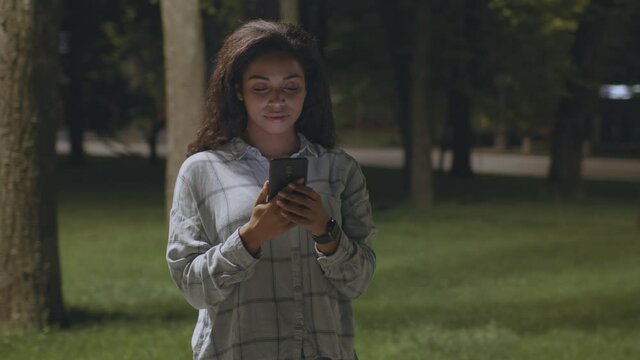 Online life. 360 degree tracking shot of young cheerful african american woman networking on smartphone in evening park