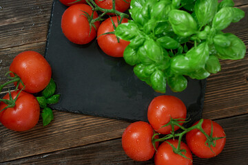 Fresh ripe red tomatoes on a cutting board with fresh basil on a wooden background. Freshly picked red tomatoes and basil  leaves for cooking. top view