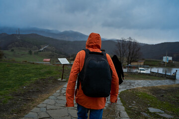 Naklejka premium A person in an orange raincoat with a backpack walks in the rain in the mountains