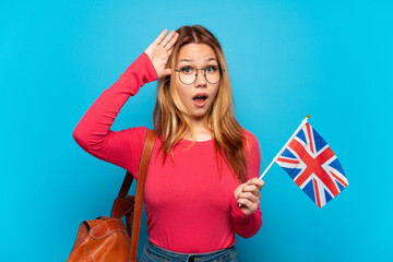 Young girl holding an United Kingdom flag over isolated blue background with surprise expression