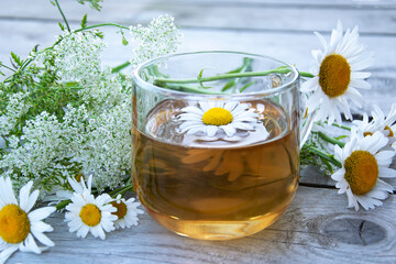 Chamomile tea close-up. Summer still life with wildflowers and chamomile drink in a glass cup. Floral background.
