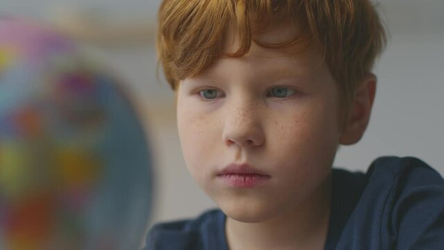 Interesting geography. Close up portrait of cute little redhead boy searching globe at home, looking at world map