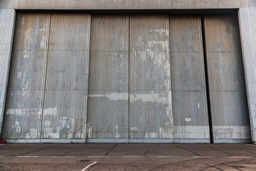 The facade of a large metal hangar with a gate.