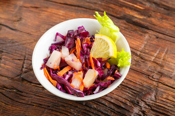 White plate with cole slow salad on a wooden background decorated with herbs.