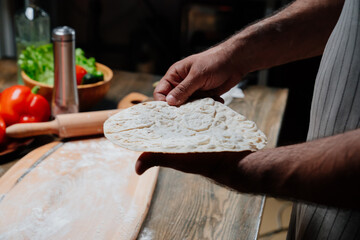 men's hands hold a thin flatbread. Cooking pizza, noodles or pitta at home