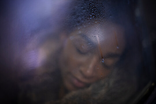 Serene young woman with eyes closed at wet window