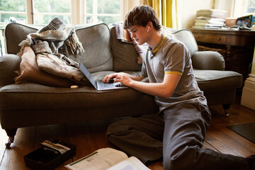 Focused teenage boy with laptop studying in living room at home