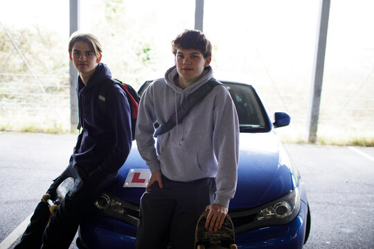 Portrait teenage boys with skateboards on car with learner permit