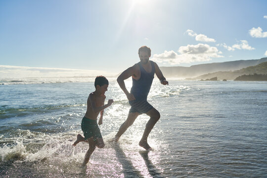 Happy father and son running in sunny ocean surf