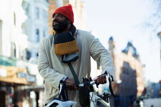 Man in stocking cap and scarf with bicycle on city street