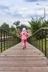 Fototapeta na wymiar A little child is running away on wooden pathway with a fence outdoors in the park