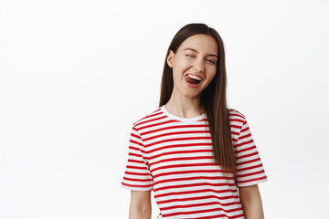 People lifestyle. Portrait of beautiful girl winking and showing tongue positive, happy face expression of young woman in casual t-shirt, white background