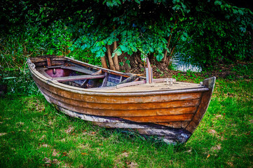 Old wooden rowing boat lying abandoned at the edge of a pond on a meadow.