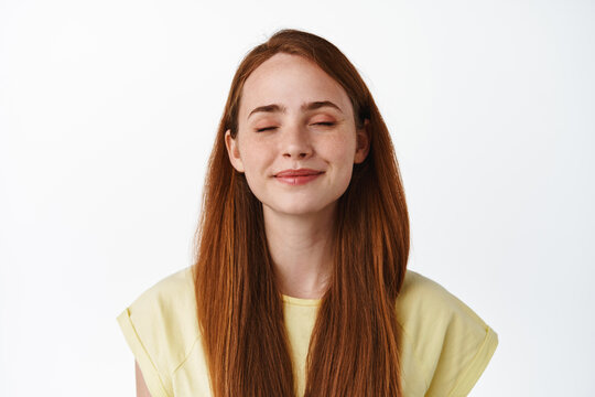 Close up of smiling ginger girl dreaming, close eyes and imaging something, picturing beautiful thing, daydreaming or remember, standing over white background