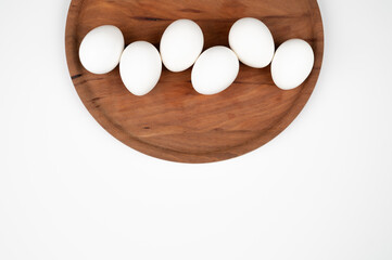 Top view of white eggs on a round wooden plate isolated on white. Organic eggs and healthy nutrition concept