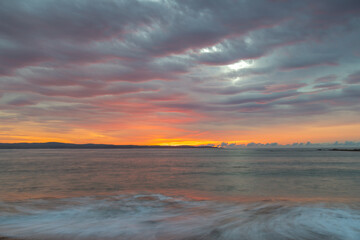 Fototapeta na wymiar Cloud covered sunrise seascape tinged with pink