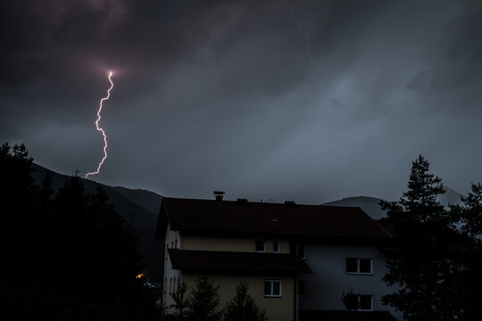 Blitze &uuml;ber einem Haus zwischen B&auml;umen