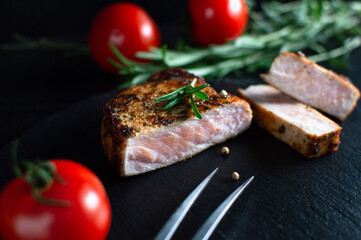 Roasted meat steak sprinkled with spices and tomatoes on black background. Still life, close-up