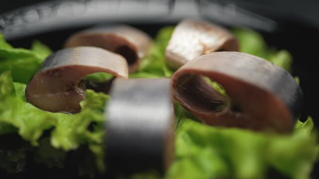 Close up herring in chunks with greens are rotating on the plate on black background. Healthy food clean eating selection.