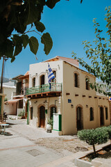 Old greek style building in Malia, town of Greece. Agiou Dimitriou street in old town. Greek flag blown by the wind.
