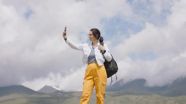 Tourist takes pictures with mobile phone camera. Young woman traveler with backpack shoots video. Travel blogger takes selfie on smartphone camera in mountains