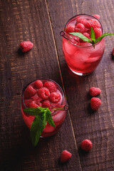 Fresh ice cold berry juice drink with mint, summer raspberry lemonade in two glass with straws on brown wooden background, angle view selective focus