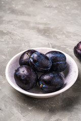 Fresh ripe plum fruits with water drops in wooden bowl on stone concrete background, angle view