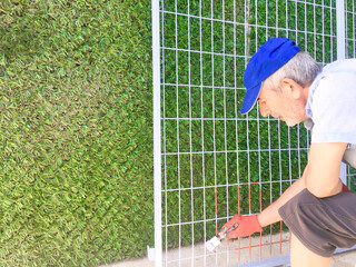 Mature man paints ironwork with paintbrush applying primer to the metal.