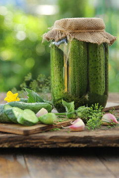 Preservations, conservation. Salted, pickled cucumbers in a jar on an old wooden table in the garden. Summer, sunny day. Cucumbers, herbs, dill, garlic. Rustic. Background image, copy space,vertical