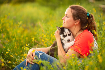 Young woman in a T-shirt hugs a husky puppy at sunset outdoors. The relationship between dog and owner