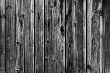 Black and white background photo of an old worn wooden fence made of planks.