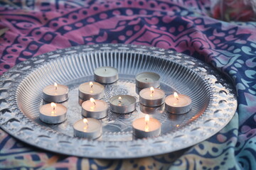 small burning candles on a silver tray and a colored pink blanket with a mandala