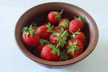 Fresh strawberries in a brown clay plate on a white background