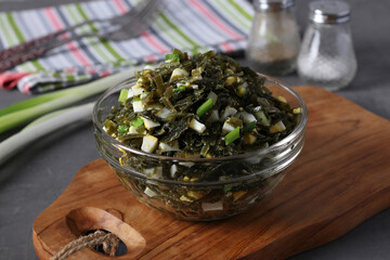 Salad with kelp, egg and green onions in a transparent bowl on wooden board. Close-up