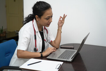 A south Indian female doctor in 30s with laptop and prescription board with white coat and red...