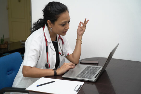 A South Indian Female Doctor In 30s With Laptop And Prescription Board With White Coat And Red Stethoscope In White Background.Online Medical Consultation