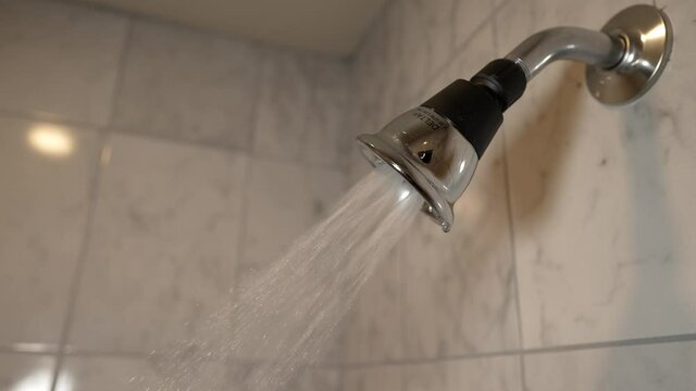 This slow motion video shows a shower head turns on and water ejecting in a modern, clean shower.