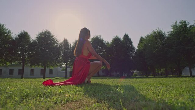 A girl in a long red dress is sitting on the lawn.Red Helium 8K