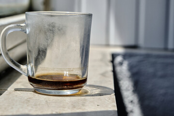 A cup made of glass material and remanings of the tea and it is standing on marble window sill and cup reflection and shadow on the sill with isolated background.