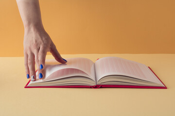Book in woman hand on orange and beige background. Minimal business concept.