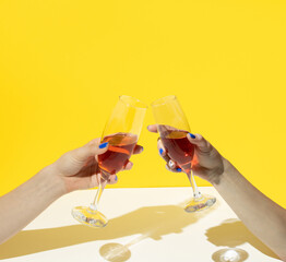 Glasses of drink in hands on yellow and white background. Minimal party arrangement.
