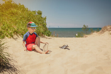 Fototapeta na wymiar Boy sitting on a dune at Indiana Dunes National Park, Chicago skyline in background