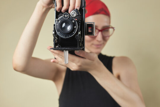 Adorable young woman holding and using an old 35mm film camera, smiling and enjoying taking pictures with an old school camera