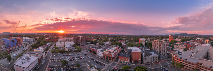 Fototapeta premium Aerial sunset view of downtown Charlottesville, Virginia with new construction office apartment building, city market parking lot, parking garage and the mall with dramatic colorful purple orange sky 
